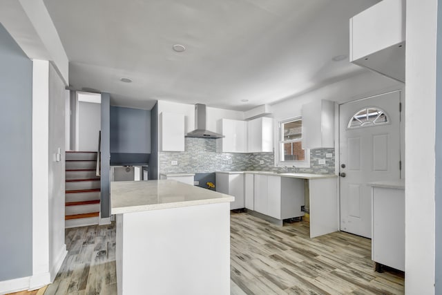 kitchen with decorative backsplash, wall chimney range hood, white cabinets, a center island, and light hardwood / wood-style floors