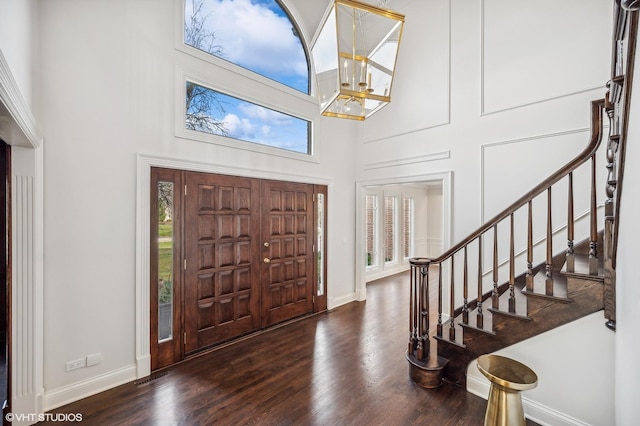 entrance foyer featuring dark hardwood / wood-style flooring, a towering ceiling, and an inviting chandelier