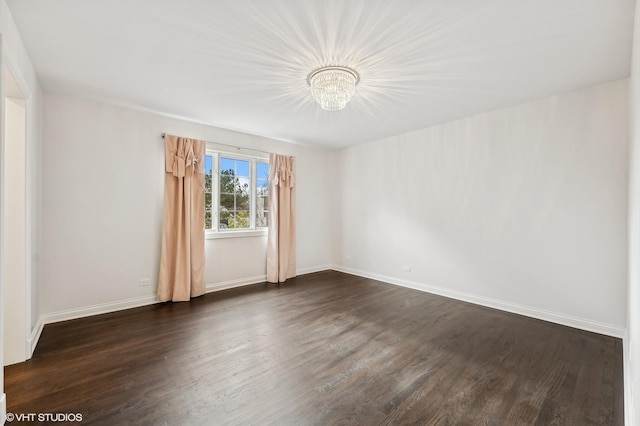 spare room featuring a notable chandelier and dark wood-type flooring