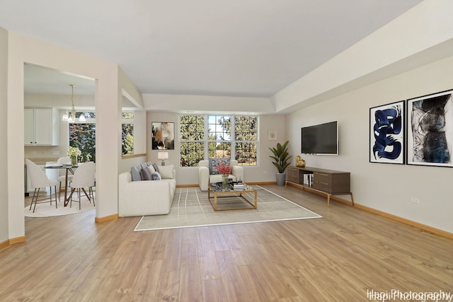 unfurnished living room featuring baseboards, a notable chandelier, and light wood-style flooring