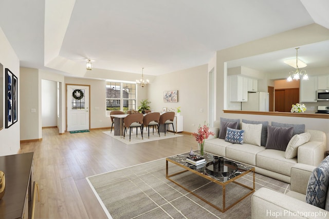 living area featuring baseboards, a raised ceiling, an inviting chandelier, and light wood finished floors