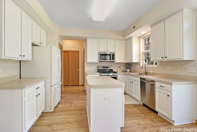 kitchen featuring a kitchen island, a sink, stainless steel appliances, light wood-style floors, and white cabinetry