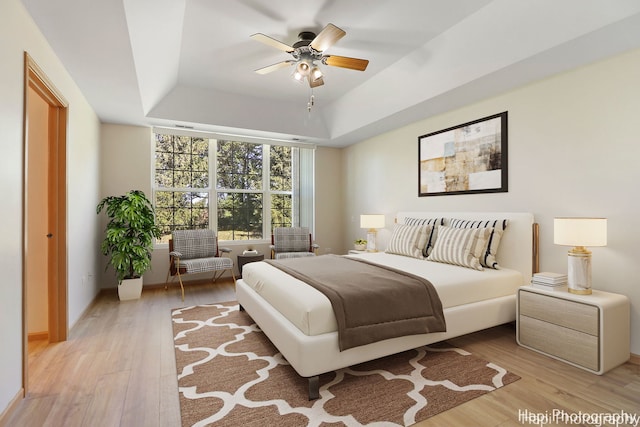 bedroom with ceiling fan, light wood-style floors, and a tray ceiling