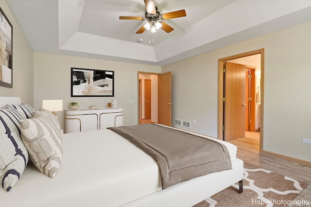 bedroom with a tray ceiling, visible vents, light wood finished floors, and ceiling fan