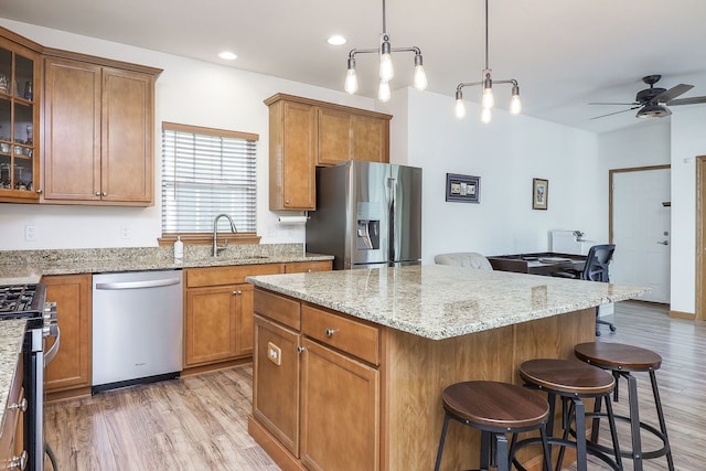 kitchen featuring a breakfast bar, sink, light wood-type flooring, appliances with stainless steel finishes, and decorative light fixtures