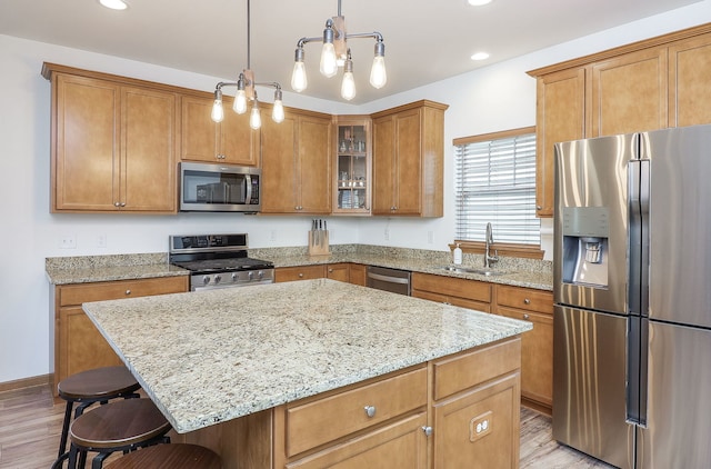 kitchen featuring sink, light hardwood / wood-style floors, pendant lighting, a kitchen island, and appliances with stainless steel finishes