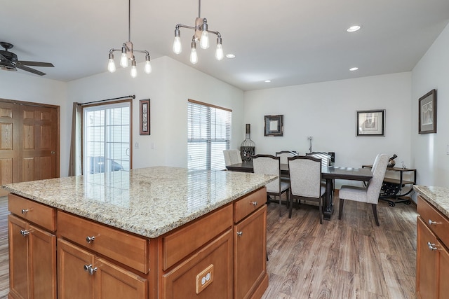 kitchen with light stone counters, ceiling fan, pendant lighting, hardwood / wood-style floors, and a center island