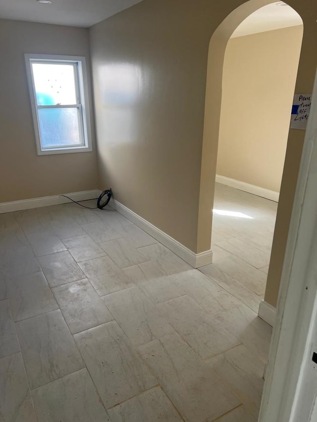 empty room featuring baseboards and arched walkways