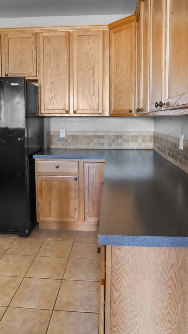 kitchen featuring light brown cabinetry, black refrigerator, and light tile patterned floors