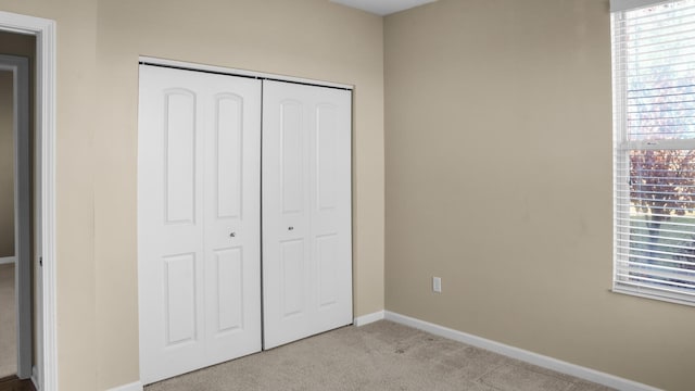 unfurnished bedroom with light colored carpet, multiple windows, and a closet