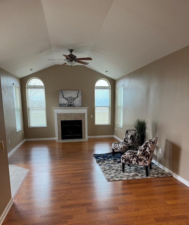 unfurnished room with ceiling fan, wood-type flooring, a tile fireplace, and vaulted ceiling