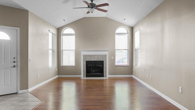 unfurnished living room featuring plenty of natural light, ceiling fan, lofted ceiling, and a tiled fireplace