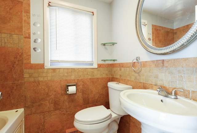 full bathroom featuring a sink, a tub to relax in, toilet, and tile walls