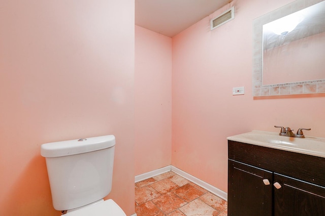 bathroom featuring visible vents, baseboards, toilet, stone tile floors, and vanity