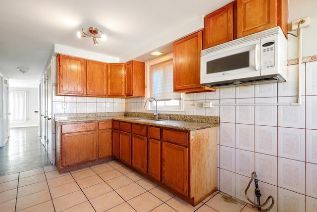 kitchen with a sink, white microwave, light tile patterned flooring, and brown cabinetry