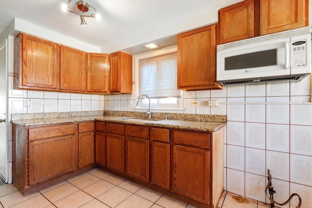 kitchen with white microwave, light stone countertops, brown cabinets, light tile patterned flooring, and a sink