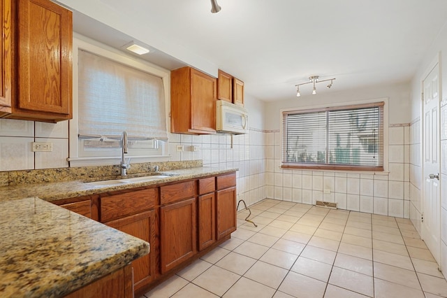 kitchen featuring brown cabinetry, light tile patterned floors, white microwave, and a sink