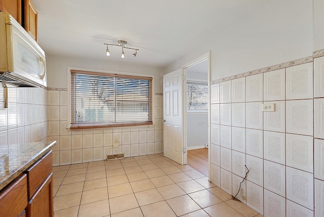 kitchen featuring light tile patterned floors, plenty of natural light, white microwave, and tile walls