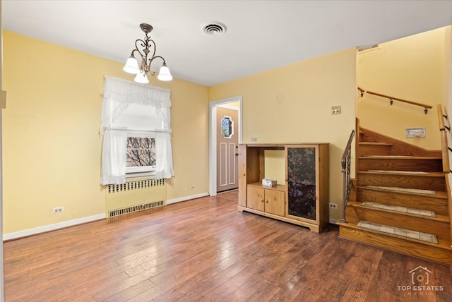 unfurnished living room with radiator heating unit, an inviting chandelier, and hardwood / wood-style floors