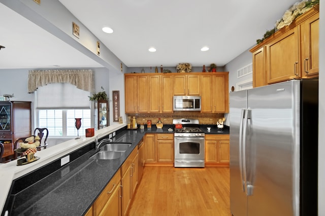 kitchen featuring sink, stainless steel appliances, dark stone countertops, decorative backsplash, and light wood-type flooring