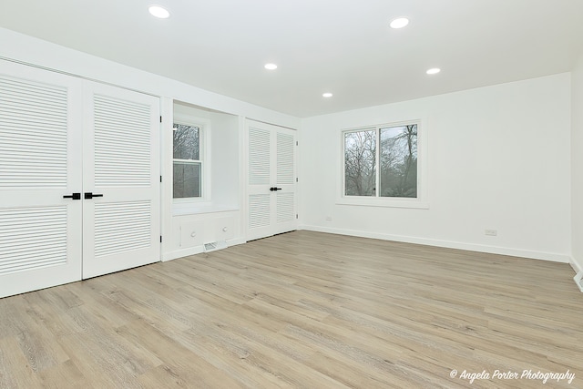 unfurnished bedroom with light hardwood / wood-style floors and multiple closets