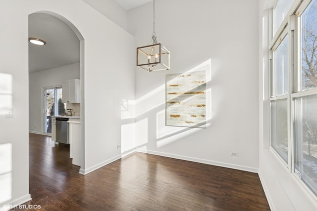 unfurnished dining area with a towering ceiling, dark hardwood / wood-style floors, and a notable chandelier