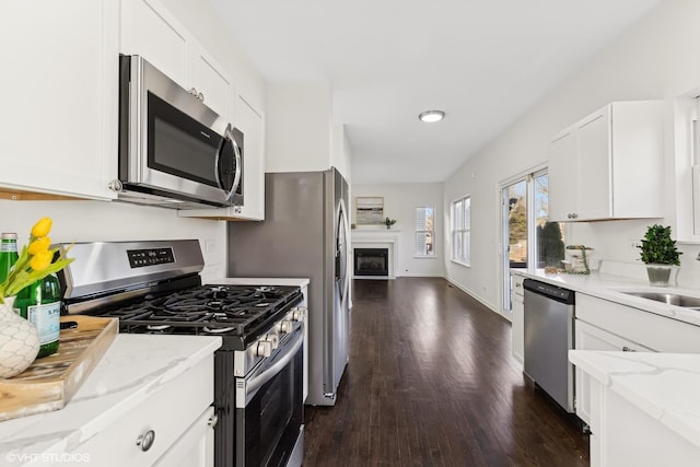 kitchen with sink, dark wood-type flooring, stainless steel appliances, light stone counters, and white cabinets