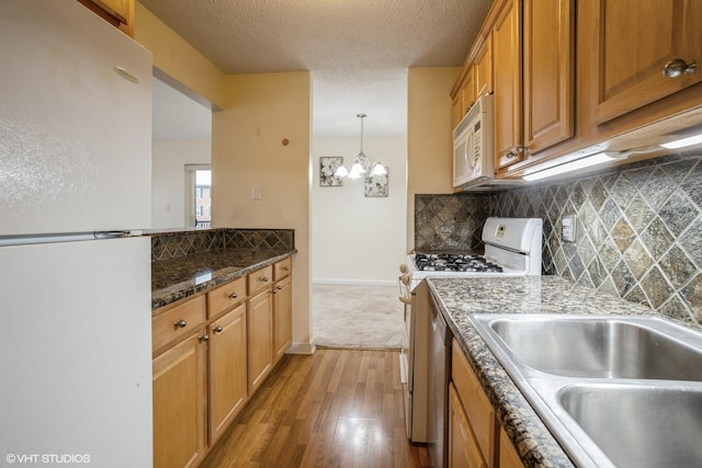 kitchen with tasteful backsplash, a chandelier, decorative light fixtures, white appliances, and light wood-type flooring