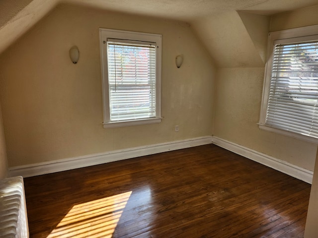 additional living space featuring a textured ceiling, dark hardwood / wood-style flooring, vaulted ceiling, and radiator heating unit