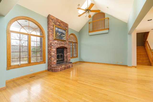 unfurnished living room featuring high vaulted ceiling, light hardwood / wood-style floors, a brick fireplace, and ceiling fan