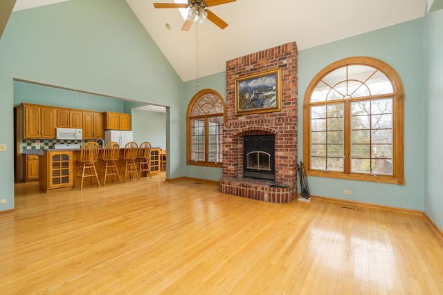 living room featuring ceiling fan, light hardwood / wood-style floors, high vaulted ceiling, and a brick fireplace