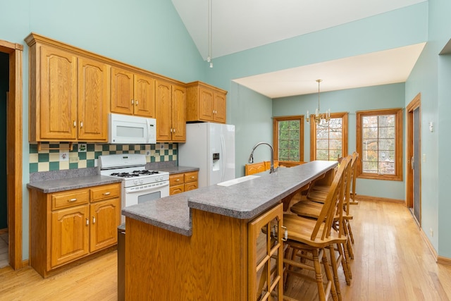 kitchen featuring white appliances, a center island with sink, sink, decorative backsplash, and a breakfast bar area