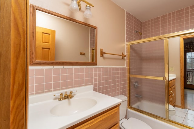 full bathroom with vanity, toilet, tile walls, and bath / shower combo with glass door