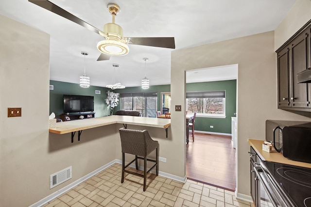 kitchen featuring dark brown cabinets, ceiling fan, light hardwood / wood-style flooring, stainless steel range oven, and a breakfast bar area