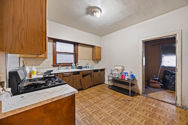 kitchen featuring black gas stove, a textured ceiling, light parquet floors, and sink