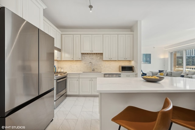 kitchen with white cabinetry, sink, stainless steel appliances, a kitchen breakfast bar, and light stone counters