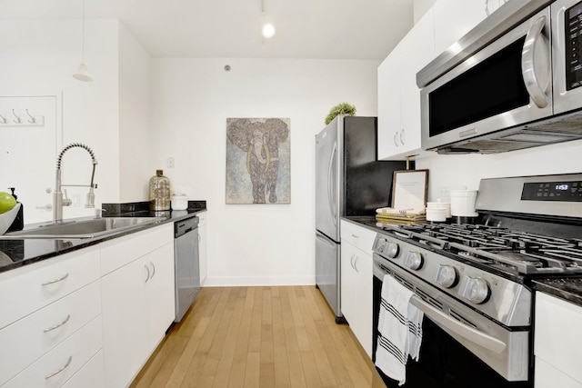 kitchen with stainless steel appliances, sink, decorative light fixtures, white cabinets, and light hardwood / wood-style floors