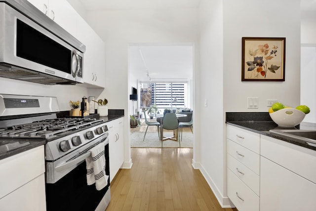 kitchen featuring white cabinets, stainless steel appliances, light hardwood / wood-style flooring, and dark stone countertops