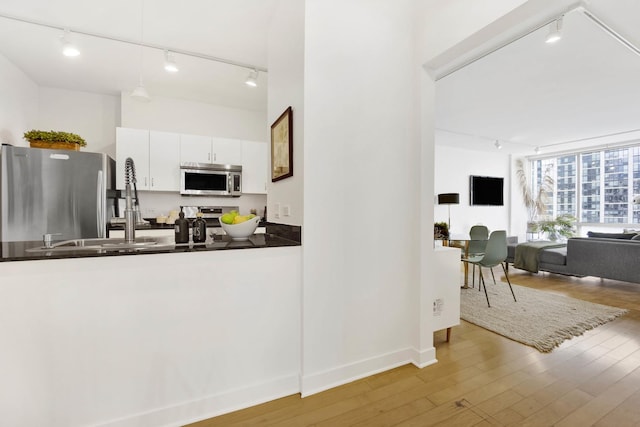 kitchen with pendant lighting, track lighting, appliances with stainless steel finishes, light hardwood / wood-style floors, and white cabinetry