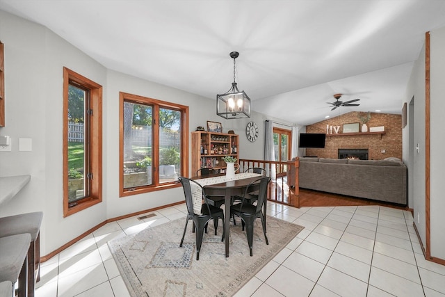 tiled dining room with ceiling fan with notable chandelier, lofted ceiling, and a brick fireplace