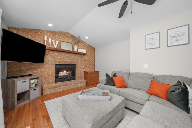 living room featuring ceiling fan, a brick fireplace, light hardwood / wood-style flooring, brick wall, and lofted ceiling