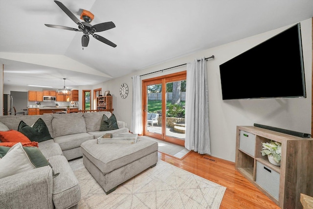 living room featuring light hardwood / wood-style flooring, ceiling fan with notable chandelier, and vaulted ceiling