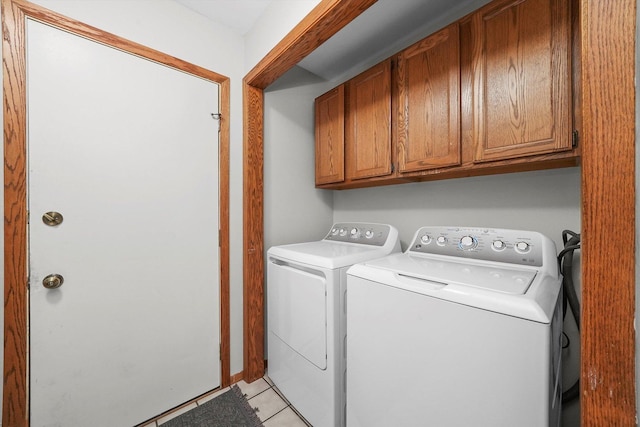 clothes washing area with washer and clothes dryer, light tile patterned flooring, and cabinets