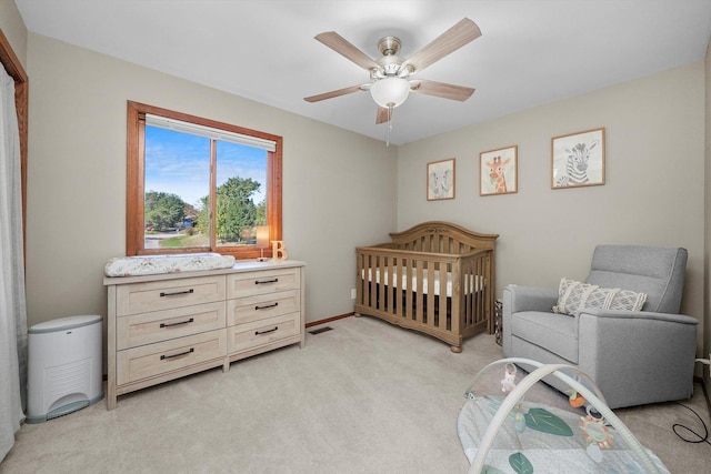 bedroom with ceiling fan, a crib, and light carpet