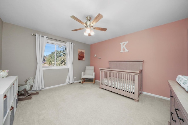 bedroom with ceiling fan, light colored carpet, and a nursery area