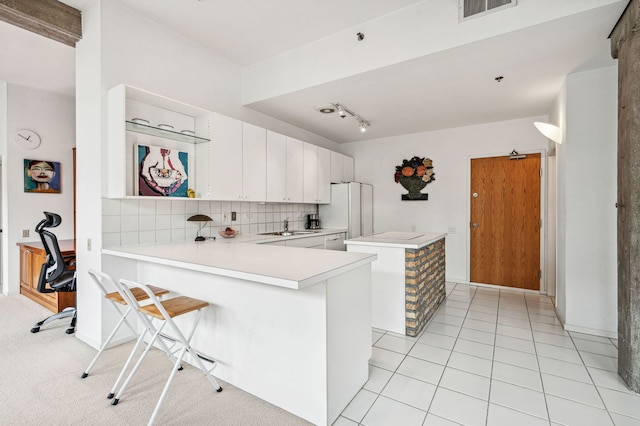 kitchen with tasteful backsplash, white cabinets, freestanding refrigerator, a peninsula, and light countertops