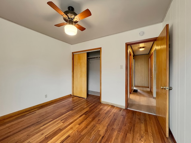 unfurnished bedroom with hardwood / wood-style floors, ceiling fan, wood walls, and a closet