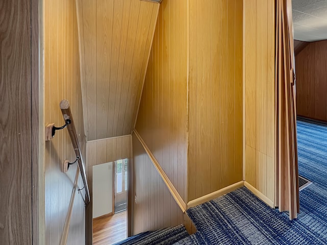 stairway with hardwood / wood-style floors, wood walls, and vaulted ceiling