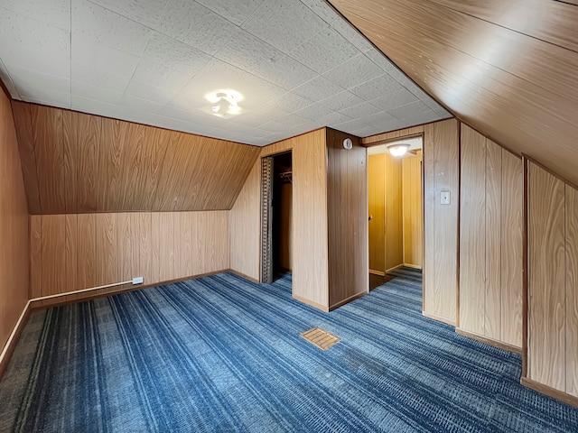 bonus room featuring dark colored carpet, wood walls, and vaulted ceiling