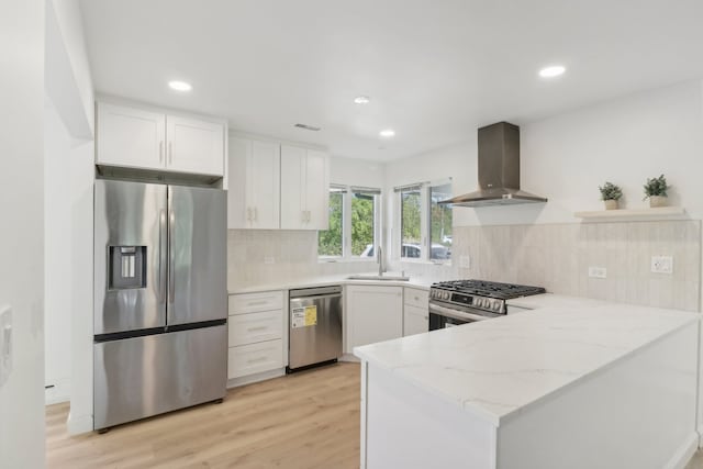 kitchen with appliances with stainless steel finishes, white cabinetry, wall chimney exhaust hood, and light stone counters